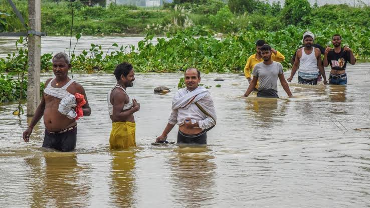 A family wades through floodwater carrying water pots, Bihar